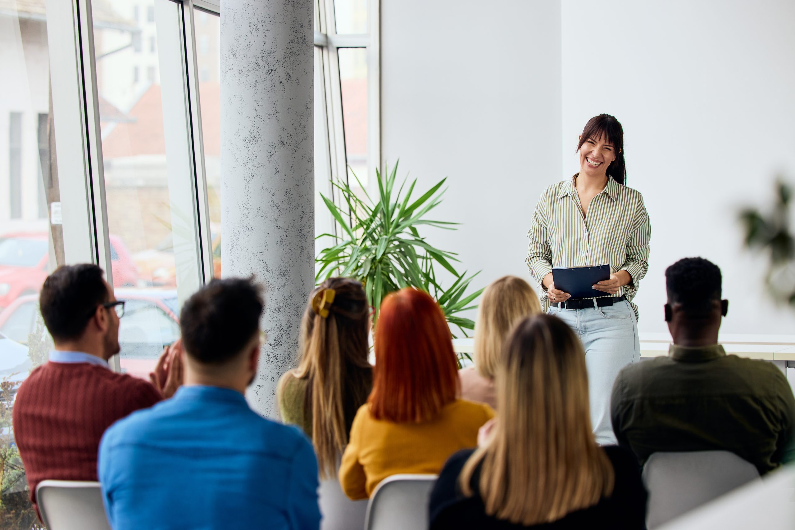 Woman speaking with a tablet to a diverse group of attentive seated listeners.