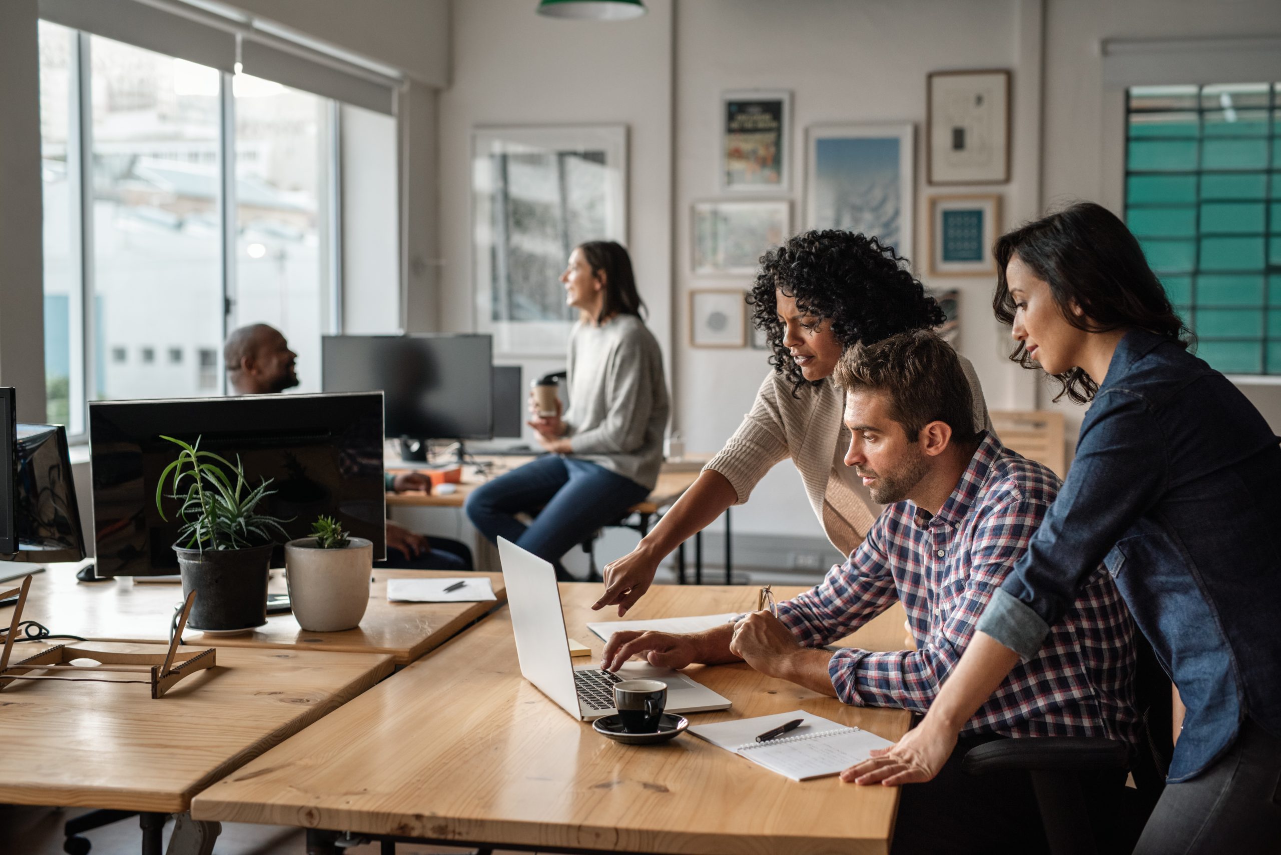 High-performing teams; Focused group of diverse young designers working on a laptop together at a desk in their startup office